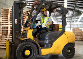 Warehouse worker wears safety helmet driving forklift truck in pallet factory. Skilled male logistic engineer working in shipping storage manufacturing lifting, moving and unloading cargo for delivery