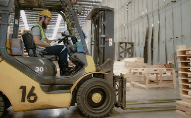 Warehouse worker wears safety helmet driving forklift truck in pallet factory. Skilled male...