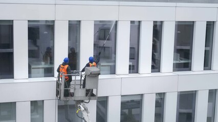 Two workers wearing safety harness wash office building facade at