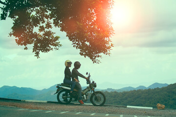 couples wearing safety helmet sitting on small enduro motorcycle against beautiful natural mountain scene at khaoyai national park thailand
