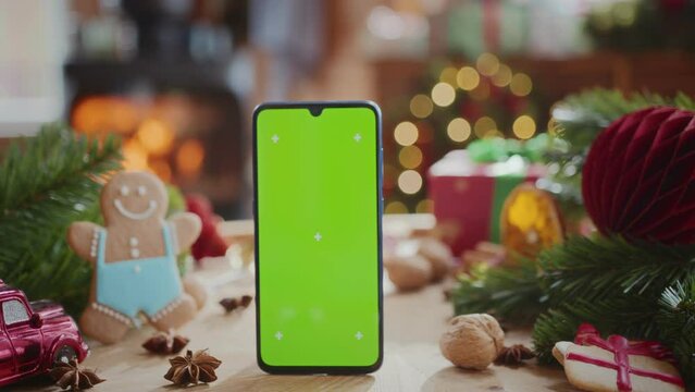 smartphone with green screen chroma key display with motion trackers on table with fir tree branches, gingerbread men and christmas decoration. burning fireplace and flashing lights on background
