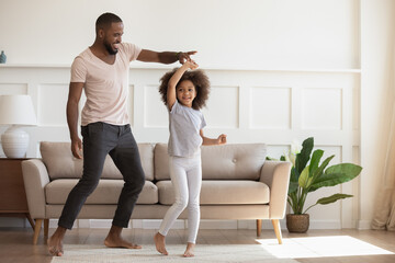 Excited loving African American smiling father twisting cute little kid daughter. Happy small girl...