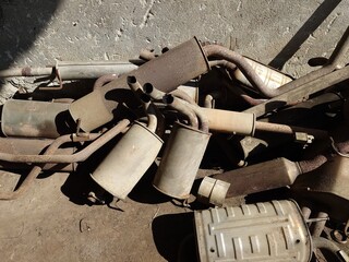 A pile of old rusted car exhausts, silencers, or tail pipes in the backyard of an auto repair shop....