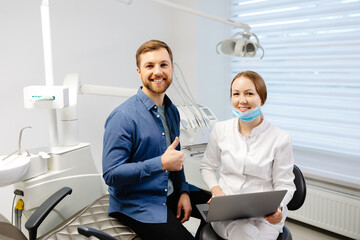 A handsome young man is talking to a female doctor at a dental appointment in a bright, beautiful...