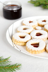 Homemade Linzer shortbread cookies with jam sprinkled with powdered sugar on white plate. Christmas festive beautiful holiday pastries, sweet treat. Christmas tree branches on a light background