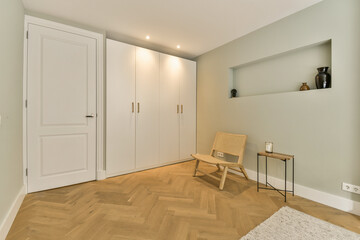 a room with wood flooring and white closets on the right side, there is a wooden chair in front of the door