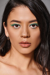 Naklejka premium portrait of beautiful asian woman with brunette hair and shimmery eye makeup on grey background