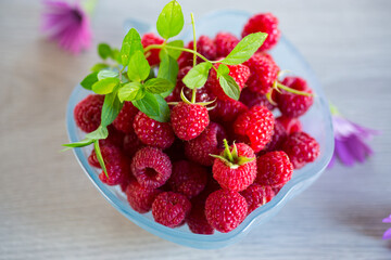 Fresh ripe raspberries in a glass bowl on wooden table.