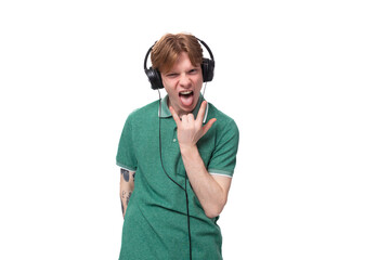 young cheerful slender student european man with red hair in a green t-shirt listens to loud music in headphones