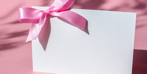 white gift card with pink ribbon bow isolated on pink pastel color background with shadow mi 