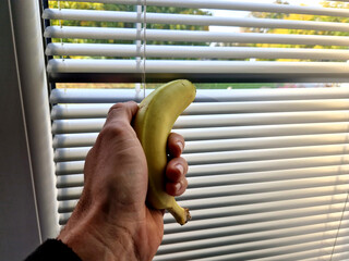 a man holds a banana in his hand and crushes it in a closed window sadistically and needlessly. he...