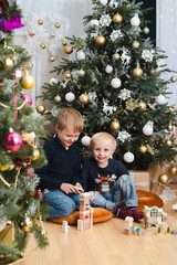 Two brothers sitting together on the floor and playing with wooden blocks under the christmas tree - blonde caucasian boys spending time together