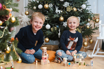 Two brothers sitting together on the floor and playing with wooden blocks under the christmas tree...