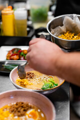 chef cooking Asian noodle soup, ramen with chicken, tofu, vegetables and egg in bowl