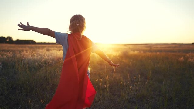 superhero girl runs across the field. happy family kid concept. a girl in a superhero costume runs along the mountain in the middle of a large field under the rays of sunlight. kid in dream suit