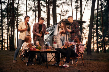 Evening time, by the table. Group of friends are together in the forest