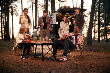 Evening time, by the table. Group of friends are together in the forest