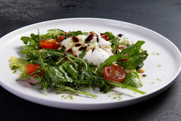 Salad with arugula, tomato and burrata cheese on a dark background.