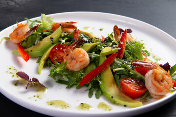 Salad with arugula, tomato, avocado and shrimp on a dark background.