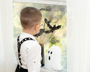 Halloween concept. No face. The baby's hands near the window, against the background of a vase with dry branches and black paper bats. Close-up. Background.