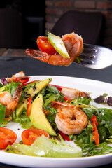 Salad with arugula, tomatoes, avocado and shrimp on a fork.