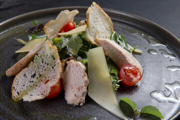 Salad with pieces of meat, tomatoes and cheese on a dark background.