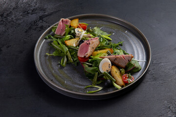 Salad with pieces of fried tuna on a dark background.