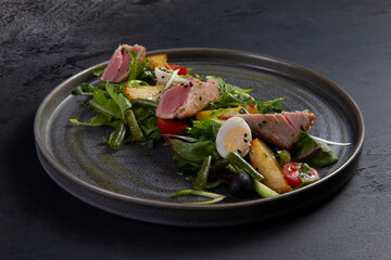 Salad with pieces of fried tuna on a dark background.