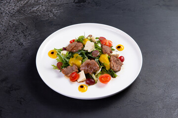 Salad with pieces of beef, tomato and cheese on a dark background.