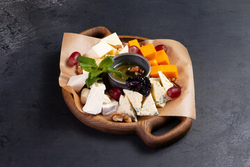 Assorted cheeses in a wooden plate. On a dark background.