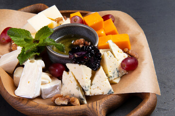 Assorted cheeses in a wooden plate. On a dark background.