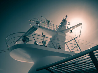 Ein mit Radarantennen gespickter Mast auf einen modernen Kreuzfahrtschiff, im Hintergrund die strahlende Sonne, farbreduzierte Aufnahme