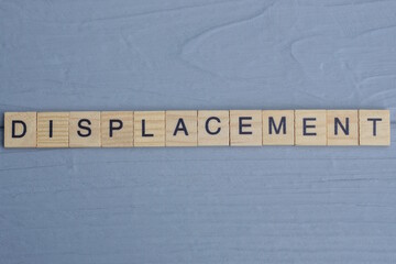 text the word displacement from brown wooden small letters with black font on an gray table