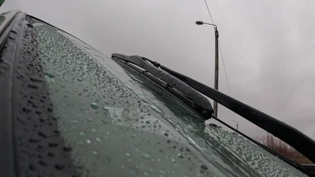 Close-up windshield with rain drops and car wipers passing. Closeup glass on rainy summer day outdoors