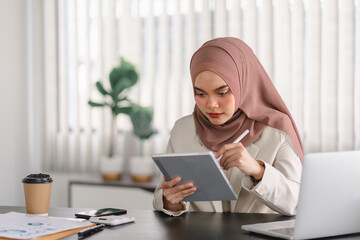 Asian Muslim businesswoman using a digital tablet while working indoors.