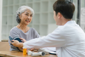 Fototapeta premium Young male doctor using digital tonometer check blood pressure for senior woman.