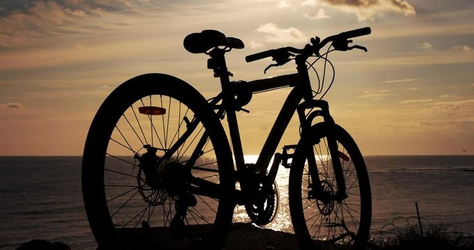Silhouette of bicycle against the sea background at sunrise