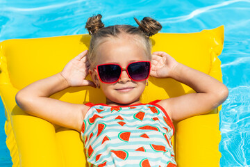 Cute little girl lying on inflatable mattress in swimming pool with blue water on warm summer day on tropical vacations. Summertime activities concept. Cute little girl sunbathing on air mattress - obrazy, fototapety, plakaty