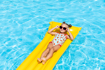 Cute little girl lying on inflatable mattress in swimming pool with blue water on warm summer day...