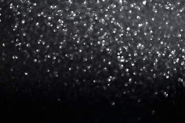 Blurred and defocused silver glitter bokeh on black background