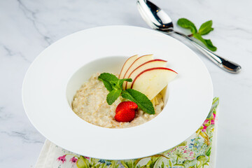 apple porridge with mint and strawberries in a white plate, side view