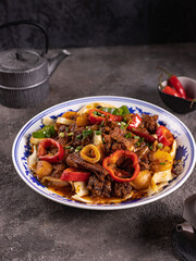 noodles with bell pepper, potatoes, meat and herbs in a plate with a pattern side view