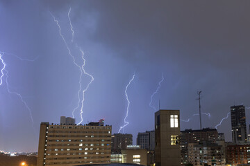 Stormy sky with several huge lightning bolts striking the ground on the outskirts of a city over...