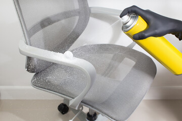A man cleans the chair armrest with a sprays foam cleaner.