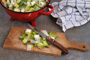 Poireaux crus coupés en morceaux avec un couteau sur une planche à découper en bois en gros plan