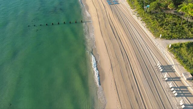 aerial footage of the coast of the Atlantic ocean with hotels and luxury condos in the city skyline at sunrise, palm trees, blue sky and clouds at Bal Harbour Beach in Miami Beach Florida USA