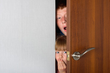 The children, a brother and a sister, peek curiously from behind the door of the room.