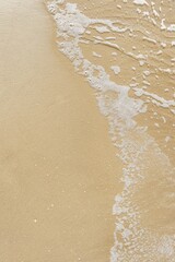 Fototapeta na wymiar Sparkling waves hitting the shore on the beach, sand beige background, vertical image.