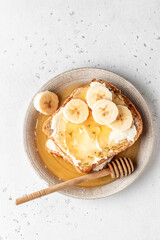 Toasts with butter, banana slices and honey on light background. Homemade breakfast sandwich close up with text space. Simple food. Top view