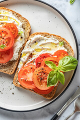 Sandwiches with tomatoes, cream cheese, olive oil and basil on a plate on white marble background close up. Traditional mediterranean food. Top view